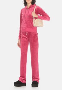 Tuta in velour rosa con felpa con zip e pantaloni con coulisse. Combinato con una piccola borsa beige e scarpe con plateau nere.