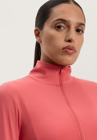 Priliehavý, vysoký golier s rozopínaním v jasne ružovej farbe, vyrobený z hladkého, elastického materiálu. Má čistý a elegantný dizajn.