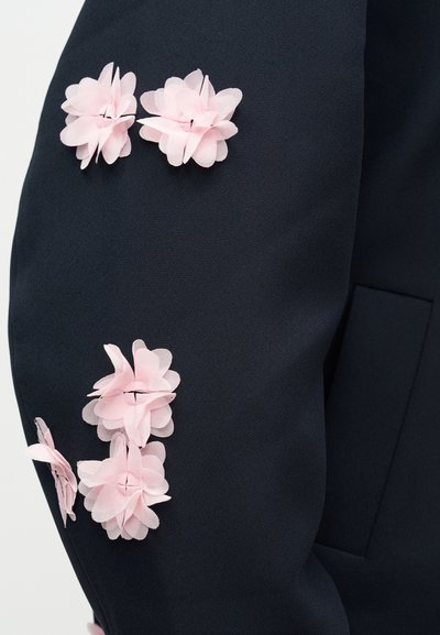 Haină din stofă bleumarin, împodobită cu multiple flori moi din stofă roz pal, cu petale stratificate și textură fină.