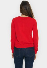 Pull rouge à col rond, à manches longues et avec un ourlet côtelé. Associé à un jean en denim bleu foncé avec des poches arrière.