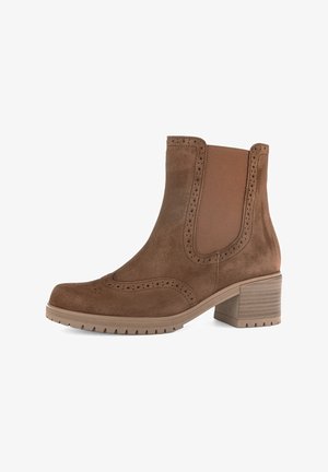 Brown suede ankle boot with elastic side panels, decorative brogue perforations, and a chunky, ridged heel. Textured surface with smooth accents.