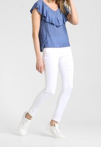 Top blu, a maniche corte con scollatura arricciata, abbinato a jeans skinny bianchi e sneakers bianche. Tessuto morbido, design semplice, senza motivi.
