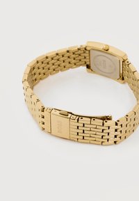 Ρολόι χειρός από μέταλλο με χρυσό τόνο, με συνδεδεμένο βραχιόλι και κούμπωμα χαραγμένο με το "BOSS" σε λευκό φόντο.