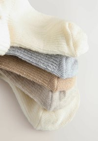 En stapel med tre strumpor i mjuk stickad kvalitet. Färger: ljus grädde, grå och beige. Har ribbade strukturer och rundad tådesign.