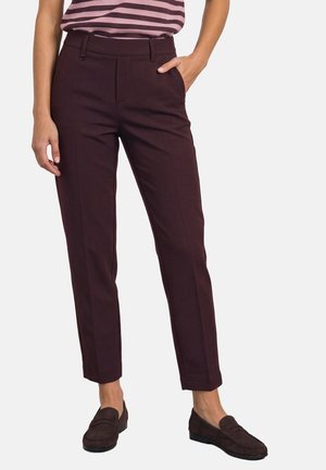 Femme portant un pantalon droit bordeaux foncé avec des poches latérales et des mocassins assortis, associé à un haut rayé rentré.