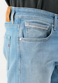 Jasnoniebieskie dżinsy z denimu z skórzaną naszywką w talii, pięcioma kieszeniami i kontrastowymi detalami w stębnowaniu.
