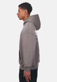 Kapuzensweatshirt in Taupe mit einer Vordertasche, gerippten Bündchen und Logodetail auf der Rückseite. Weicher Stoff mit lockerer Passform und seitlichen Schlitzen.