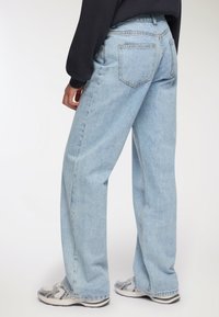 Jeans alta vita di colore azzurro chiaro con design a gamba larga, rifiniti con una texture sbiadita e due tasche posteriori. Indossati con sneaker.