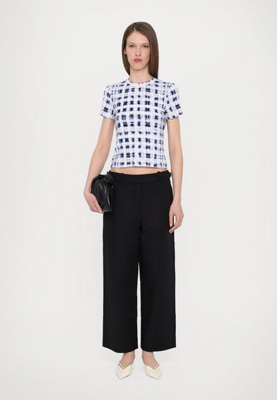 Cropped white top with blue tie-dye pattern, black wide-leg trousers, and pointed cream flats; accessorized with a black clutch.