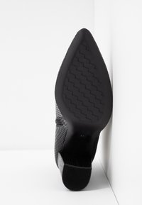 Schwarzer High Heel Schuh mit einem strukturierten synthetischen Obermaterial und einer spitzen Zehe. Die Sohle weist ein schwarzes Gummitraktionsmuster auf.