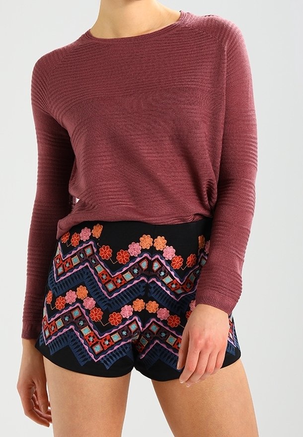 Bordeauxrotes Langarmoberteil mit strukturierten Streifen, kombiniert mit schwarzen Shorts, die mit buntem Blumen- und Zickzack-Stickdesign verziert sind.