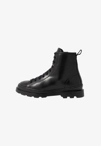 Botas de tobillo de cuero negro con un acabado suave, diseño de cordones y una distintiva suela de goma gruesa. Estilo minimalista con costuras reforzadas.