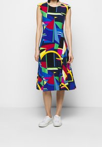 Colorful, knee-length dress made of fabric with a geometric pattern in blue, green, red, yellow, and black. Short cap sleeves and flared skirt.