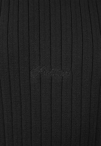 Tissu tricoté côtelé noir avec un texte brodé en cursive noire subtilement centré sur le matériau.