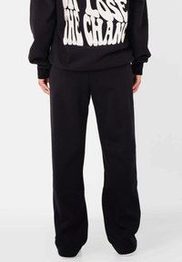 Zwarte sweatpants van zachte stof, met een relaxte pasvorm en een gladde textuur. Accenteert met een wit logo op de bijbehorende top.