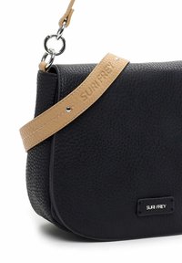 Sac bandoulière en cuir texturé noir avec bandoulière beige réglable embossée "SURI FREY" et anneaux et clous métalliques argentés.