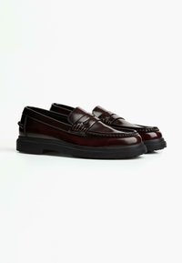 Pair of dark brown leather loafers with black rubber soles, featuring a moccasin toe and strap detail, on a white background.