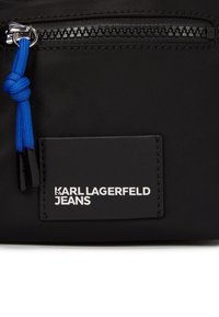 Juodas audinio maišelis su užtrauktuku, su mėlynu virvutės užtrauktuku. Juoda etiketė su balta užrašu skaito "KARL LAGERFELD JEANS."