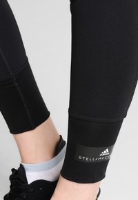 Primo piano di gambe inferiori che indossano leggings neri Adidas Stella McCartney e sneakers nere con calzini bianchi alla caviglia.