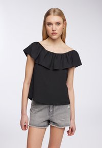 Top nero senza spalline con scollatura arricciata, realizzato in tessuto leggero; abbinato a pantaloni corti in denim grigio strappati.