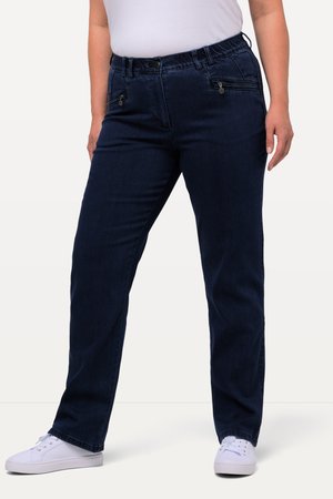 Person iført mørkeblå jeans med lige ben, lynlåslommer foran og hvide sneakers, der står mod en ensfarvet baggrund.