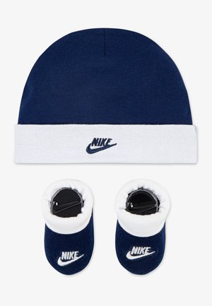Bonnet bleu marine avec un bord blanc et le logo Nike, associé à des chaussons bleu marine assortis avec des dessus blancs et le logo Nike. Matériau en coton doux.