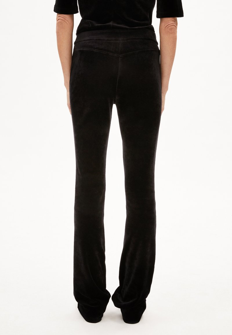 Pantaloni a zampa d'elefante in velluto nero con una texture liscia, caratterizzati da una vita alta e un design aderente, mostrati da dietro.