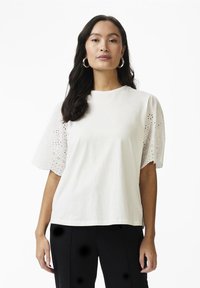 Tricou din bumbac alb cu mâneci scurte și puffate, prezentând broderii cu decupaje florale. Design drept și decolteu rotund.