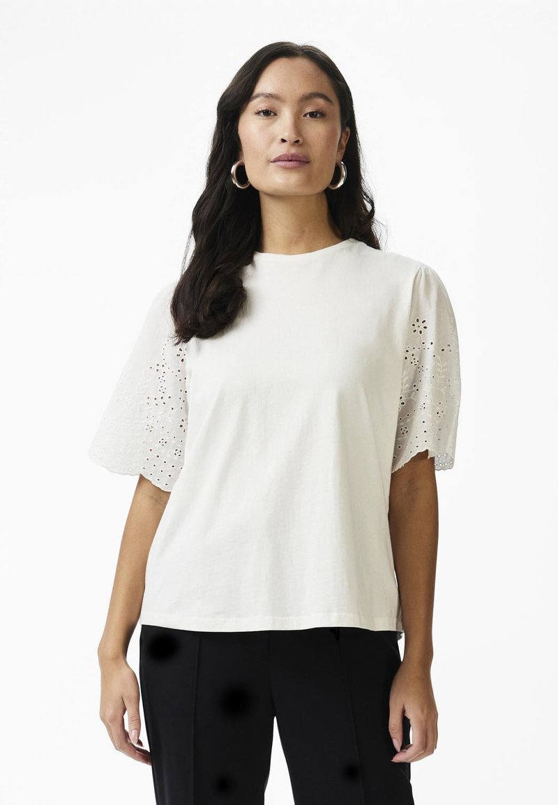 Tricou din bumbac alb cu mâneci scurte și puffate, prezentând broderii cu decupaje florale. Design drept și decolteu rotund.
