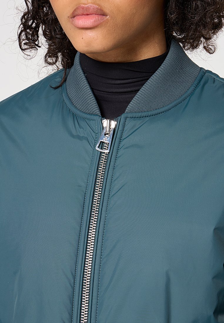 Türkiser Bomberjacke mit einem Reißverschluss vorne, geripptem Kragen und glatter Textur. Verfügt über ein silbernes Reißverschlussdetail und eine lässige, entspannte Passform.