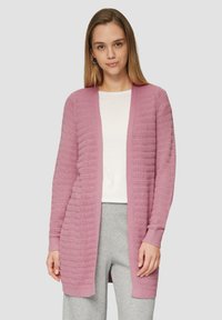Lichtroze cardigan met een gestructureerd ribpatroon, open voorkant, lange mouwen en zachte gebreide stof. Gemaakt over een witte top en grijze broek.