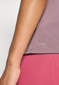 Prim-plan al unui braț purtând un top mauve DRYCELL și colanți texturați roz, evidențiind textura materialului și potrivirea îmbrăcămintei pe talie.