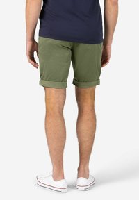 Grüne Baumwollshorts mit umgeschlagenen Säumen, kombiniert mit einem marineblauen Oberteil und weißen Sneakers. Der Stoff ist weich und hat eine glatte Textur.