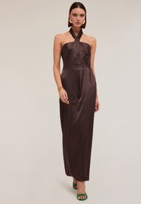 Rochie satin maro cu gât halter, cu un front drapat, siluetă ajustată și design lung până la podea. Asortată cu pantofi cu toc înalt, verzi, îmbelciți.