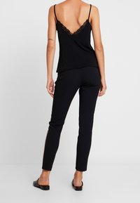 Camisole noire avec dentelle et fines bretelles, associée à un pantalon noir ajusté avec une bande latérale. Le tissu semble lisse et doux.