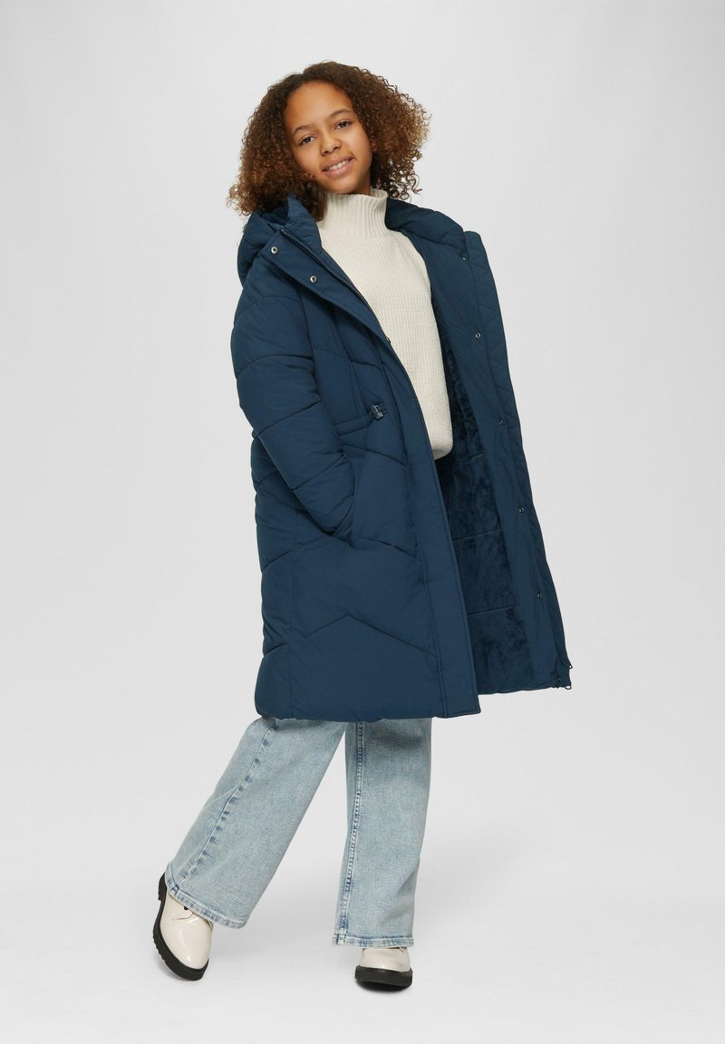 Navyblauer Daunenmantel mit Kapuze, mit einem gesteppten Design, Fronttaschen und einem weichen Futter, kombiniert mit hellblauen Schlagjeans und Schuhen.