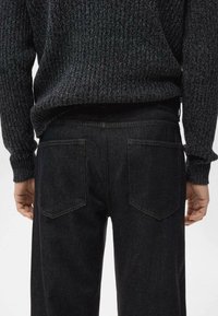 Vaqueros negros de denim con un corte recto, que cuentan con dos bolsillos traseros y una cinturilla sencilla. Combinados con un suéter oscuro texturizado.