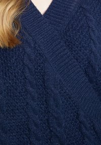 Marinblå stickad tröja med ett kabelmönster och texturerade sektioner. V-ringad design och mjuk, tjock värme.