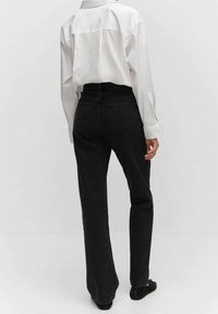 Vaqueros negros de cintura alta con piernas anchas, textura de denim y bolsillos traseros tradicionales. Combinados con una camisa blanca de botones.