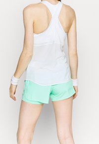 Top atlético blanco sin mangas con diseño de espalda nadadora, combinado con pantalones cortos verde menta. La parte superior cuenta con una textura de malla transpirable.