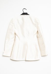 Bílý blazer s přiléhavým střihem, jediným rozparkem vzadu a černými akcenty na límci. Hladká textura, dlouhé rukávy a knoflíkové manžety.