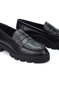 Mocasines de cuero negro con acentos de tachuelas, correa frontal texturizada y suela de goma gruesa. Punta redondeada y acabado suave.