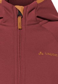 Rote Kapuzenjacke mit glatter Textur, ausgestattet mit einem metallischen Reißverschluss, kontrastierenden orangefarbenen Akzenten und einem kleinen eingeprägten Logo auf der Brust.