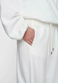 Felpa bianca con cappuccio caratterizzata da un davanti testurizzato, polsini elasticizzati e una vita con cordino. Include una tasca laterale ed etichetta del marchio.