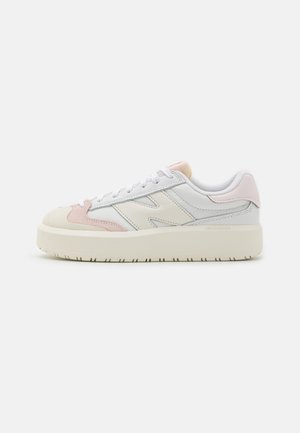 Biały niski sneaker z beżowymi i jasnoróżowymi akcentami, grubą podeszwą, sznurowaniem z przodu i naszywanym logo po boku na jednolitym tle.