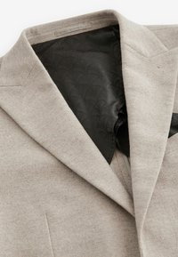 Hellbeige Fischgrätblazer mit einem schwarzen gemusterten Innenfutter. Verfügt über eine klassisch geschnittene Revers und strukturierte Schultern. Weiche Textur.