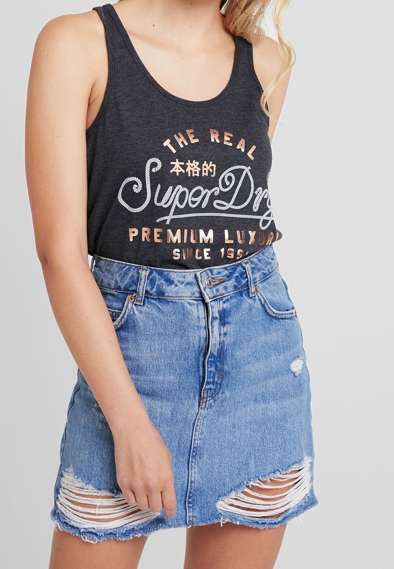 Canotta nera con lettere bianche e rosa oro, abbinata a una gonna in denim scucita con strappi e orli sfrangiati.