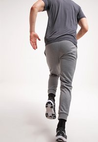 Szare sportowe dresy o zwężanym kroju i elastycznym pasie, w połączeniu z ciemnoszarym podkoszulkiem z krótkim rękawem i czarnymi trampkami.