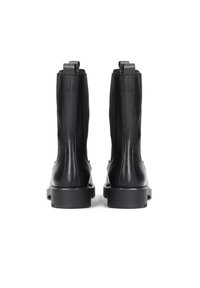 Botas de cuero negro hasta la mitad de la pantorrilla con lengüetas para tirar, costuras visibles y tacones bajos y gruesos, vistas desde atrás sobre un fondo blanco.