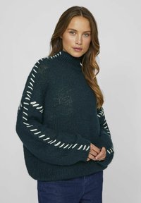 Mörkgrön stickad tröja med hög hals, med vit söm längs ärmarna och en lös, strukturerad passform.